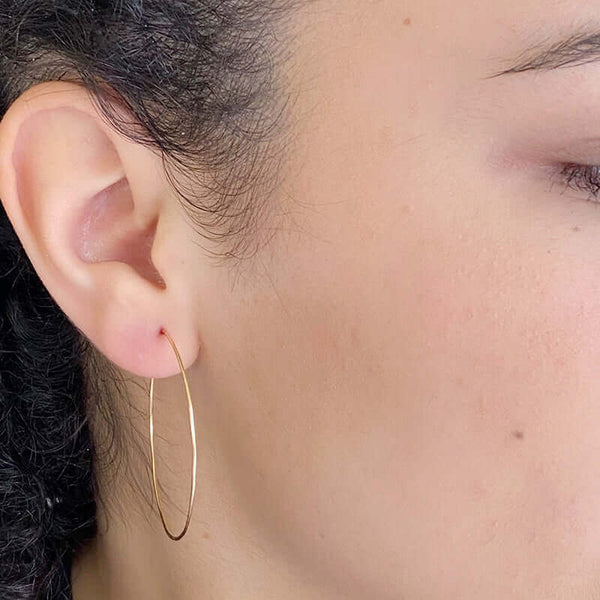 Close-up side view of woman wearing a pair of simple gold hoop earrings with loop and hook as clasp.