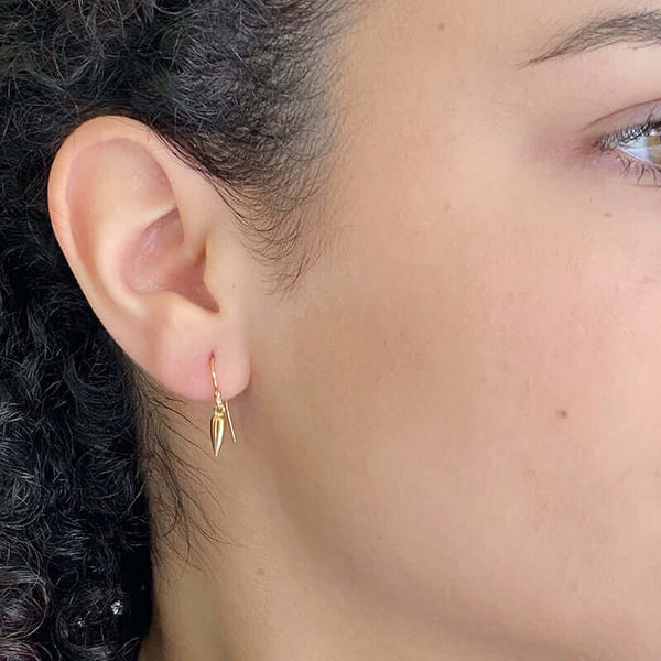 Close-up side view of a pair of gold spike earrings on earwire.