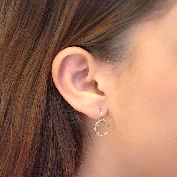 Close-up side view of woman wearing a pair of gold circle earrings on earwire.