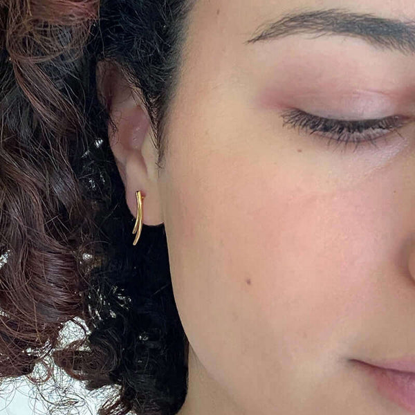 Close-up front view of woman wearing a pair of gold earrings of 2 curved swoops on posts, hanging down.