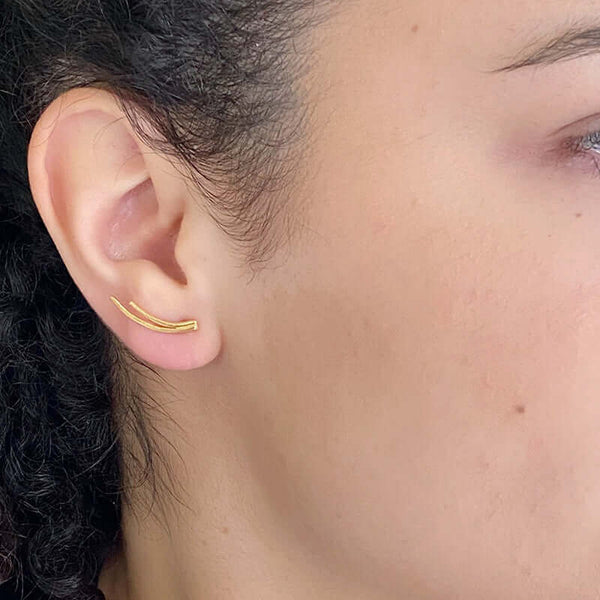 Close-up side view of woman wearing a pair of gold earrings of 2 curved swoops on posts, worn curving up.