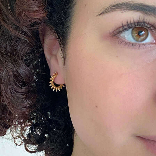 Close-up front view of woman wearing a pair of cast curved spiky gold earrings on posts.