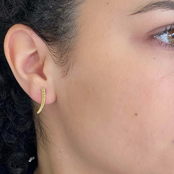 Close-up side view of woman wearing a pair of gold earrings, curved spike with serrations on posts.
