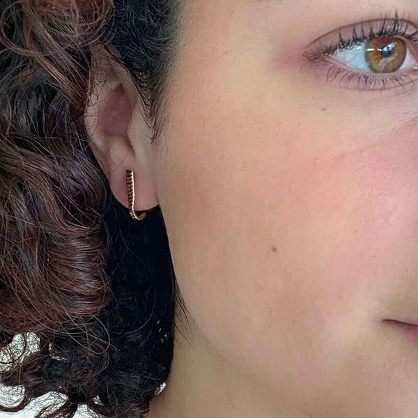 Close-up front view of woman wearing a pair of gold earrings, curved spike with serrations on posts that hooks around earlobe.