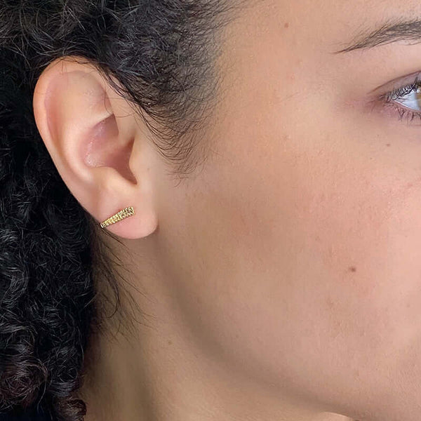 Close-up side view of woman wearing a pair of gold earrings, curved spike with serrations on posts that hooks around earlobe.
