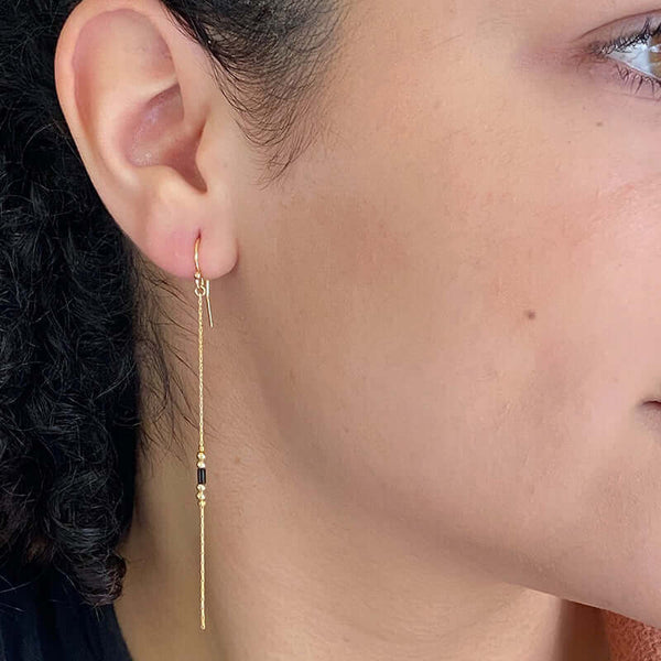 Close-up side view of woman wearing a pair of gold earrings, gold chain with black bead details.