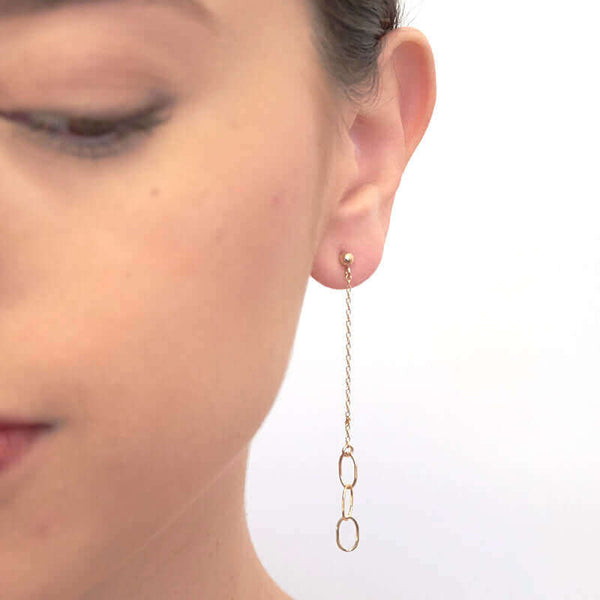 Close-up front view of woman wearing a pair of gold earrings, 3 oval links on gold chain on posts.