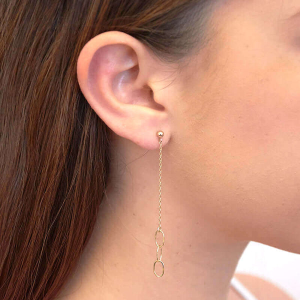 Close-up side view of woman wearing a pair of gold earrings, 3 oval links on gold chain on posts.