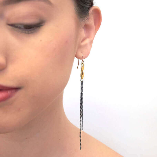 Close-up front view of woman wearing a pair of dark chain earrings, multiple dark chains hanging on gold links.