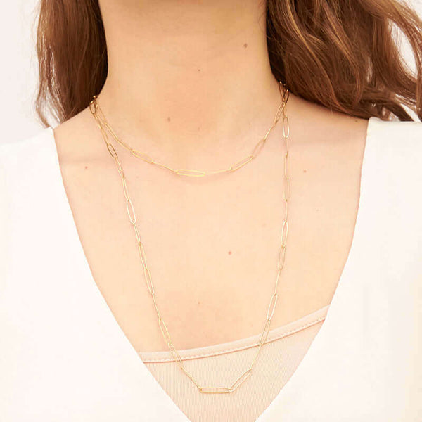 Woman wearing long gold elongated link necklace doubled to have a short loop and long loop.