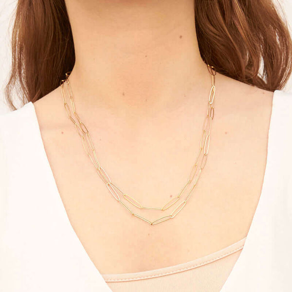 Woman wearing a long gold elongated link necklace doubled up to sit higher on chest.