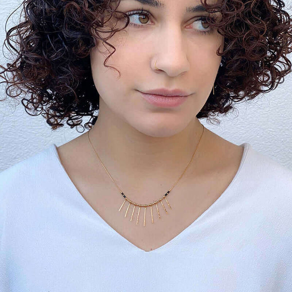 Woman wearing gold necklace with pendant of rays, worn short just below collarbone.