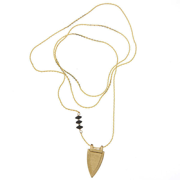Long gold necklace with shield shaped pendant and black bead accents, chain looped to show length of necklace.
