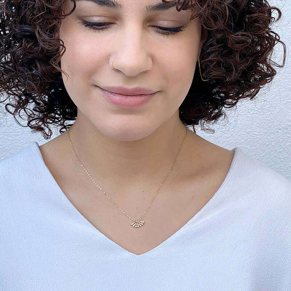 Woman wearing gold necklace with fan-shaped lace pattern pendant, inset with small diamond.