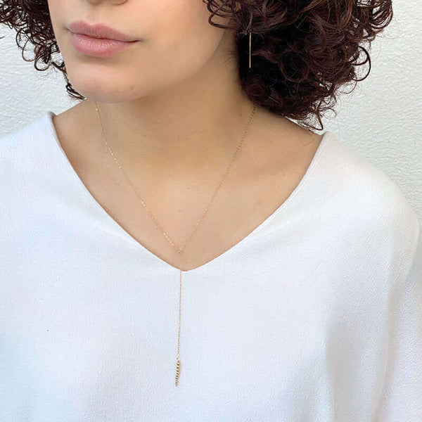 Woman wearing delicate gold chain necklace with drop pendant of small gold beads.