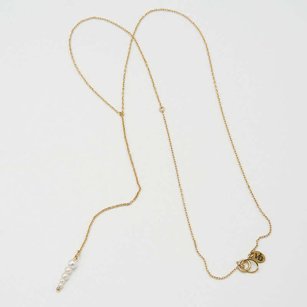 Delicate gold chain necklace with drop pendant of small pearl beads, laid out showing full length.