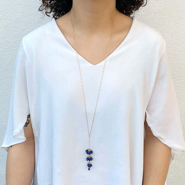 Woman wearing gold chain necklace with pendant of 3 bunches dark blue beads and single bead at end.