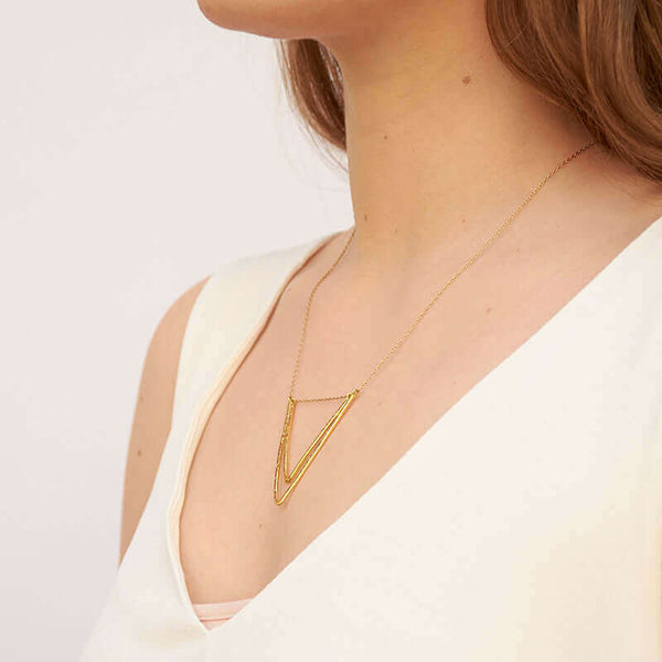 Woman wearing delicate gold chain necklace with two nested v-shaped pendants, shown form side angle.