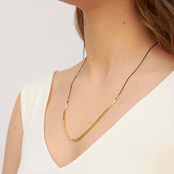 Woman wearing necklace with black upper chain and gold box chain on the bottom, shown form side angle.