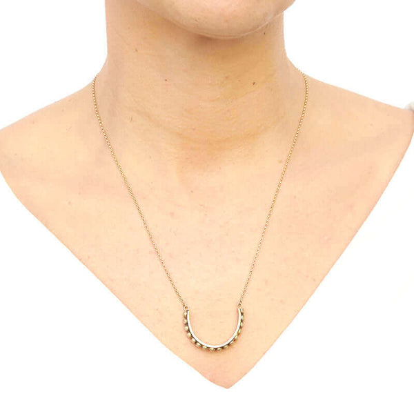 Woman wearing gold chain with half-circle beaded bar as pendant, worn long.