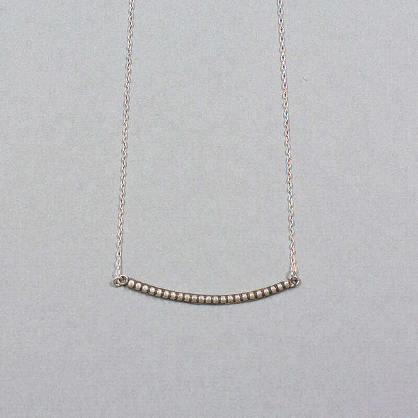 Close-up of silver chain necklace with curved beaded bar pendant.
