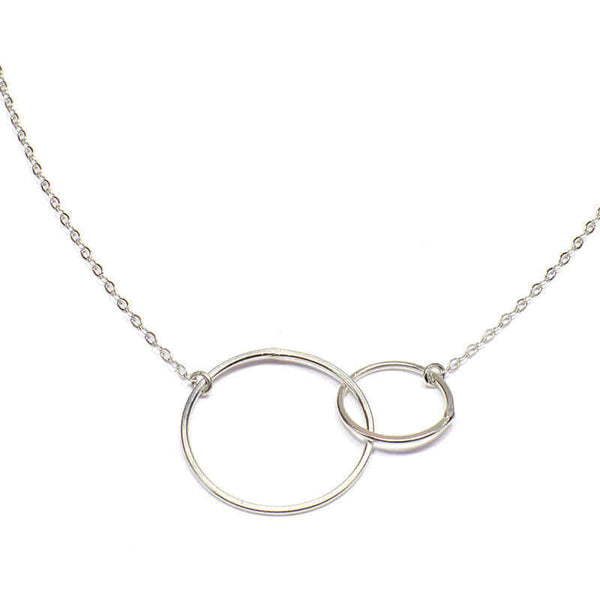 Close-up of delicate silver chain necklace with small and large interlocking circles as pendant.