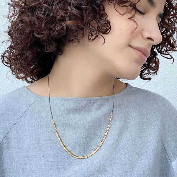 woman wearing necklace with black chain on top and flat brass curb chain in front.