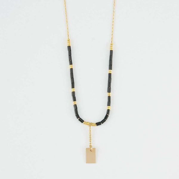 Close-up of delicate gold necklace with black and gold beads and gold rectangle drop pendant.