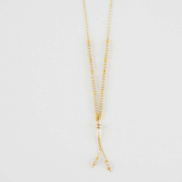 Close-up of delicate gold necklace with white and gold beads shown reverse with adjuster bead.
