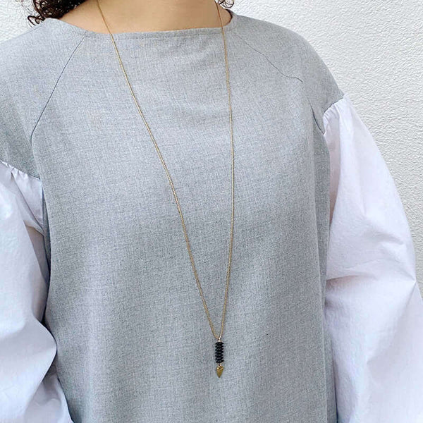 Woman wearing delicate gold chain necklace with pendant of black beads and arrowhead.