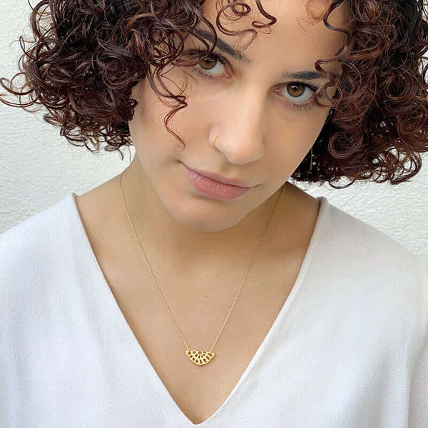 Woman wearing delicate gold chain necklace with lotus root motif pendant.