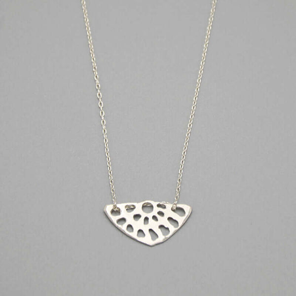 Close-up of delicate silver chain necklace with lotus root motif pendant.