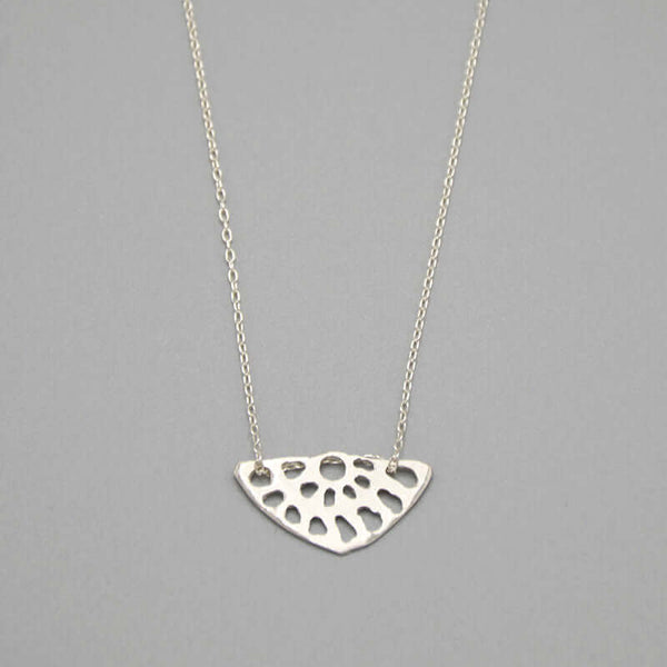 Close-up of delicate silver chain necklace with lotus root motif pendant.