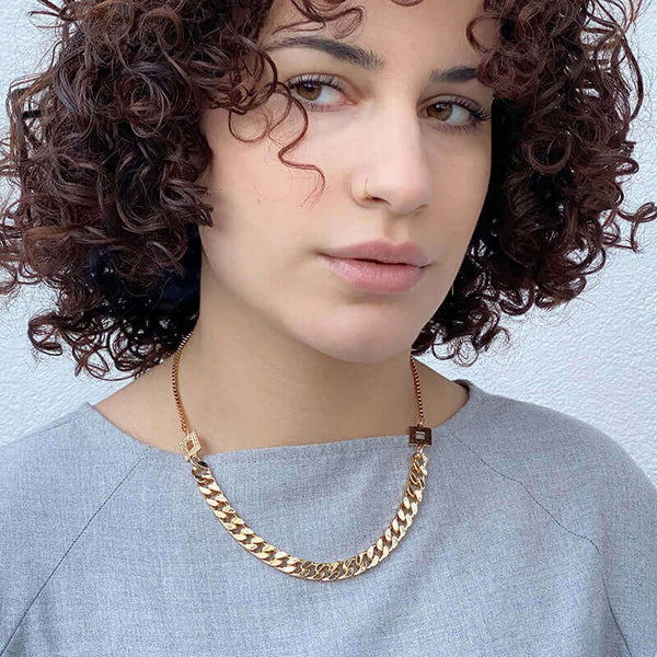 Woman wearing gold necklace with heavy curb chain on bottom and smaller box chain at top, with square link details.