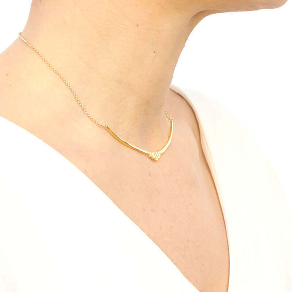 Woman wearing gold necklace with curved bar pendant with geometric native motif, shown side angle.