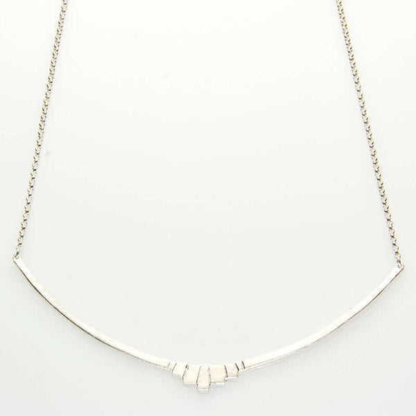 Close-up of silver necklace with curved bar pendant with geometric native motif.