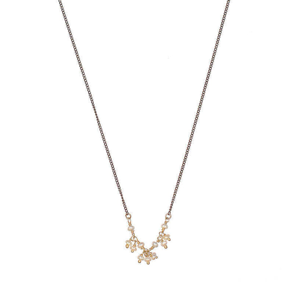 Close-up of delicate black oxidized necklace with small pearls as pendant.