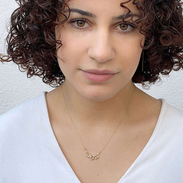 Woman wearing delicate gold necklace with small pearls as pendant.