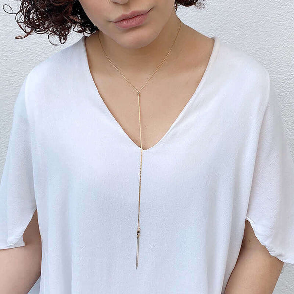 Woman wearing delicate gold chain lariat style bracelet with slider bead and black bead details near ends, worn tight.