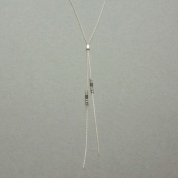 Close-up of delicate silver chain lariat style bracelet with slider bead and black bead details near ends.