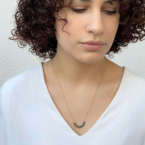 Woman wearing gold necklace with beaded curved pendant.