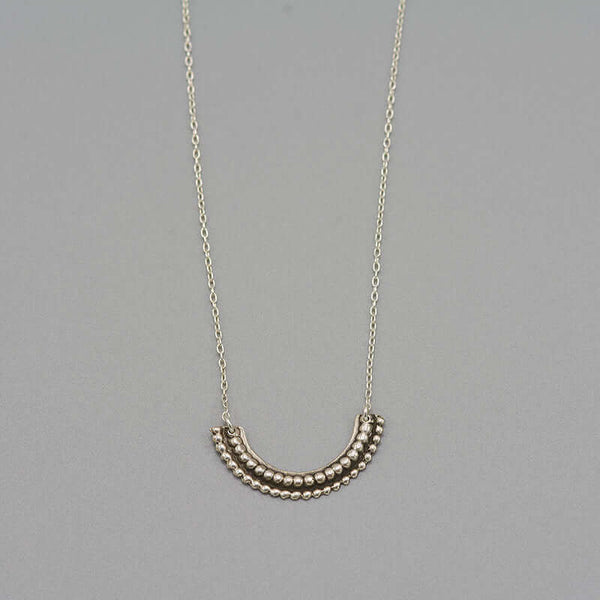 Close-up of silver necklace with beaded curved pendant.