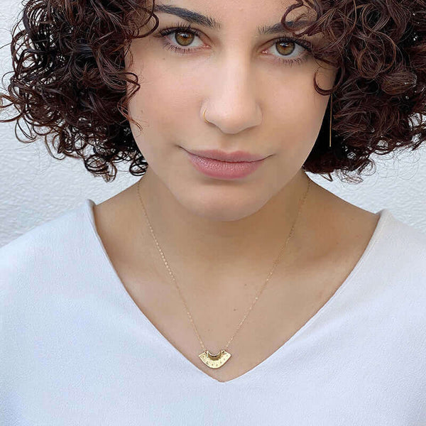 Woman wearing dainty gold necklace with fan shaped pendant.