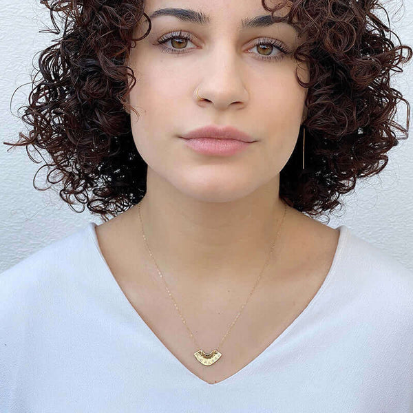 Woman wearing dainty gold necklace with fan shaped pendant with tiny diamonds.