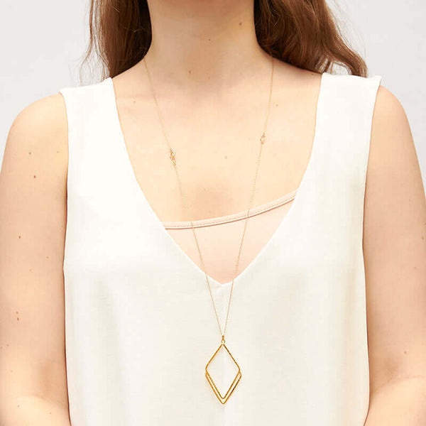 Woman wearing long gold necklace with rhombus shaped pendant.