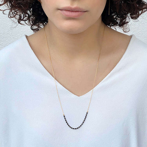 Woman wearing gold necklace with black tubes and gold beads on bottom hanging long.