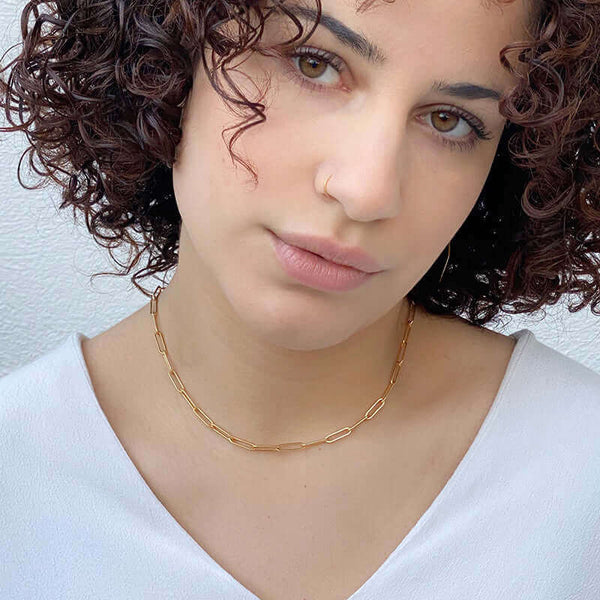 Woman wearing short gold elongated link necklace.