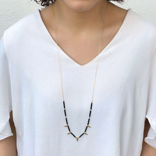 Woman wearing gold necklace with spiral black tubes and gold beads with 5 gold spikes, worn long.