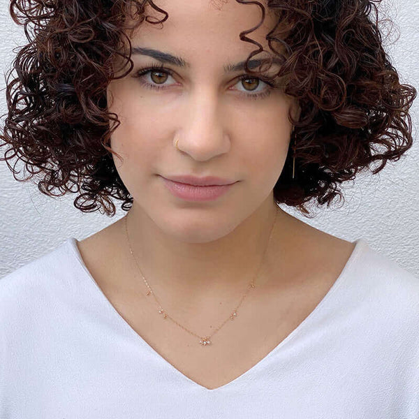 Woman wearing dainty gold necklace with details of pearls along chain and pearls as pendant.