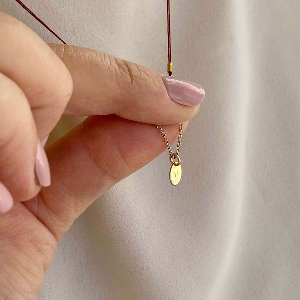 Close-up of fingers holding delicate red thread necklace with gold chain and oval pendant.